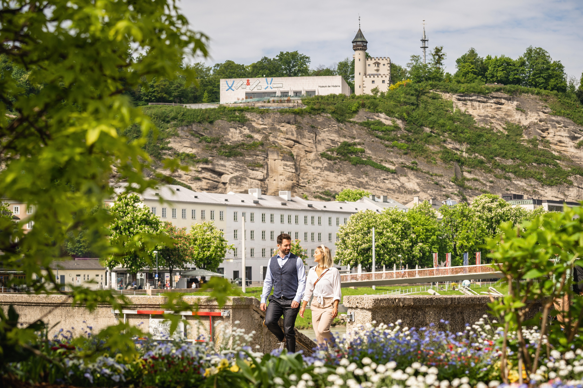 Ein Paar spaziert beim Urlaub in Salzburg durch die frühlingshafte Blumenwelt entlang der Salzach.