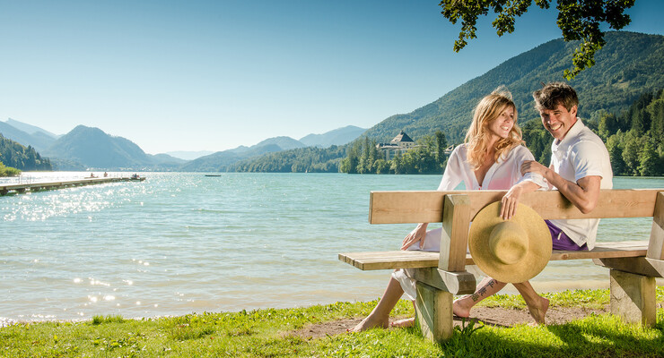 Ein Paar sitzt im Urlaub beim Fuschlsee auf einer Bank am Ufer