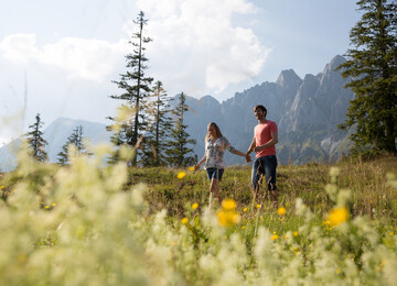 Ein Paar geht bei einer Wanderung über eine wunderschöne Wiese in der Region Salkammergut. 