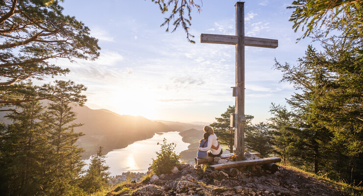 Eine Mutter sitzt mit ihrer Tochter am Gipfel des Ellmausteins und genießt den Sonneruntergang über den Fuschlsee.